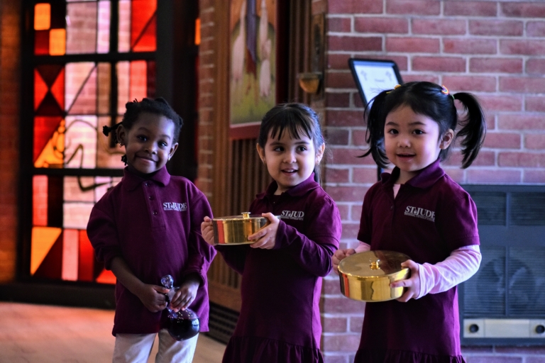 PreK 3 girls hold the bread and wine as they prepare to present the gifts during Mass